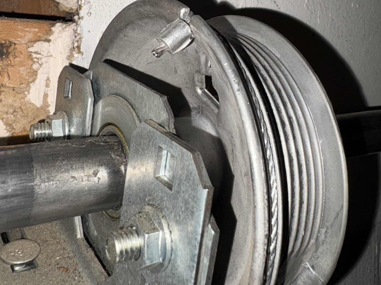 Close-up of a garage door cable drum on the torsion shaft in a Colorado Springs garage, with the lift cable wound in its grooves.