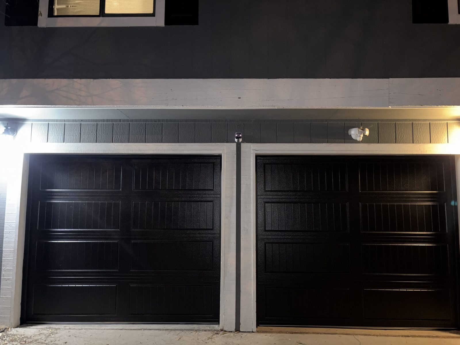 Two black carriage-style garage doors on a Colorado Springs home at night, lit by exterior lights on a cold evening.