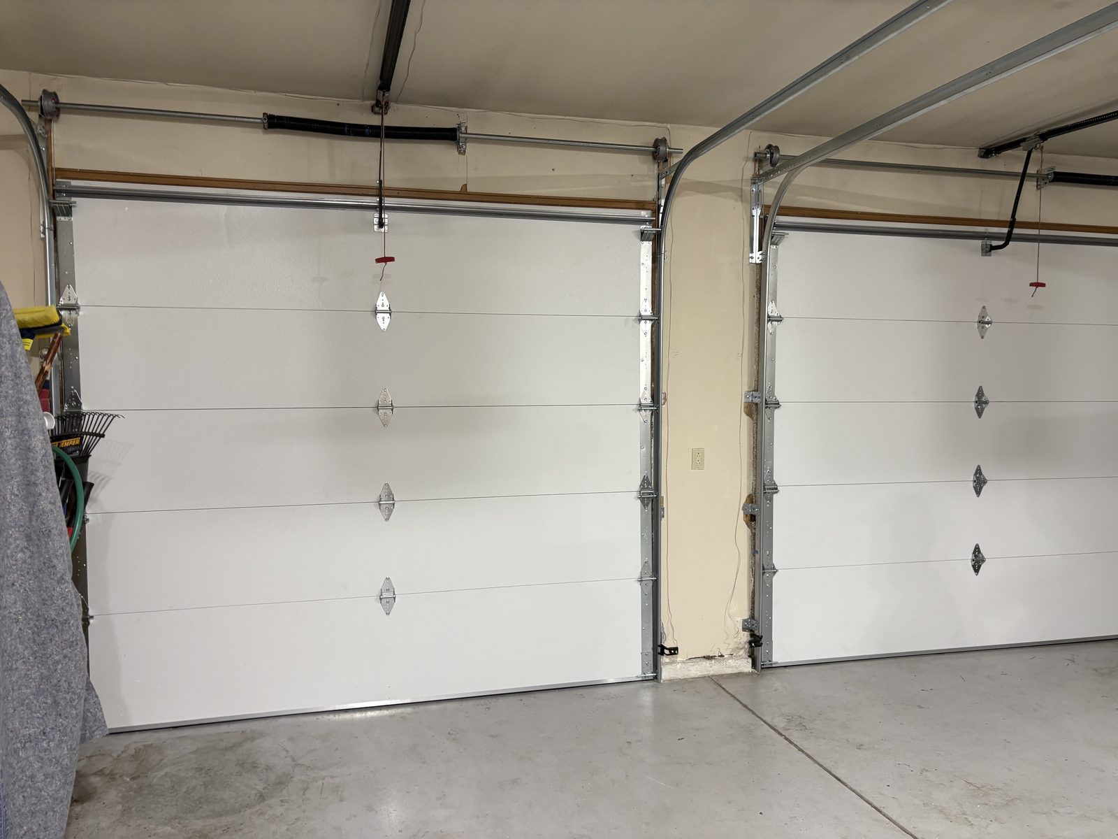 Two white steel sectional garage doors in a Colorado Springs garage, closed, with the bottom edge of each door meeting the concrete slab.